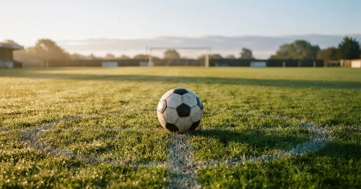 Een voetbal op de middenstip van een grasveld in het ochtendlicht