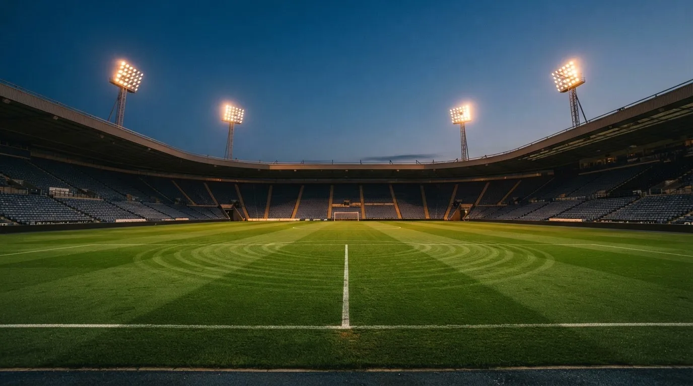 Een leeg voetbalstadion met lichtmasten bij schemering