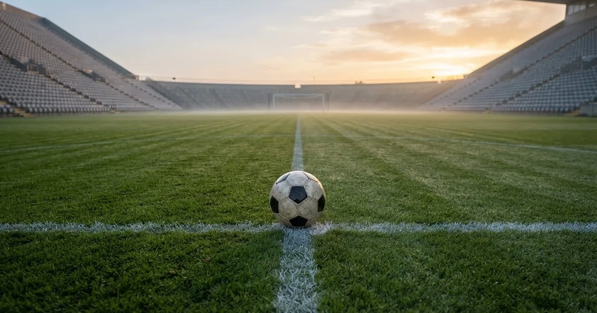 Een voetbal op de middenstip van een grasveld in het ochtendlicht