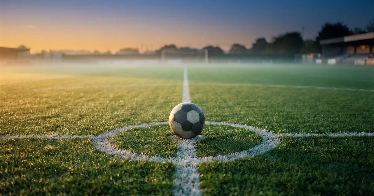 Een voetbal op de middenstip van een grasveld in het ochtendlicht