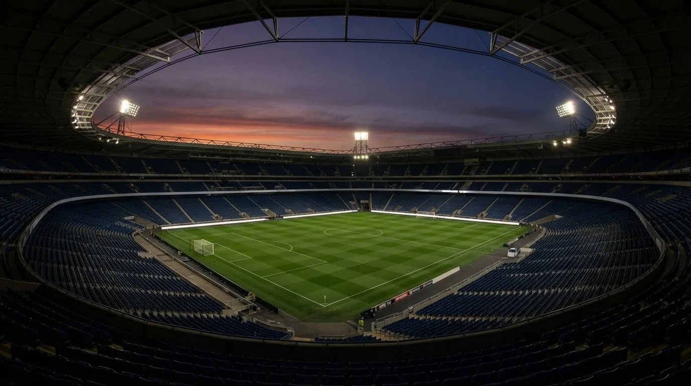 Een leeg voetbalstadion met lichtmasten bij schemering