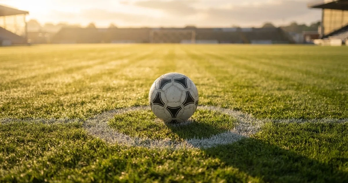 Een voetbal op de middenstip van een grasveld in het ochtendlicht